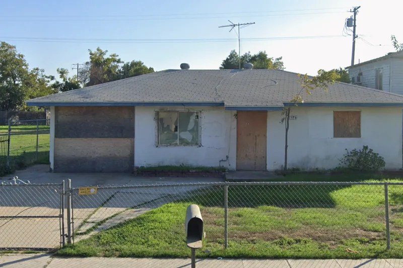 A boarded and vacant home on the Fresno County tax-sale list, plywood over the door and both front windows