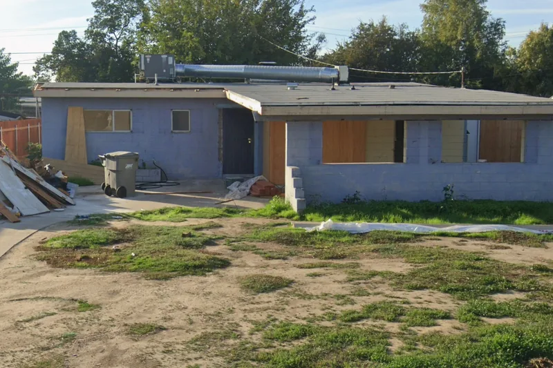 A gutted house on the Fresno County tax-sale list, every opening boarded and building debris in the yard