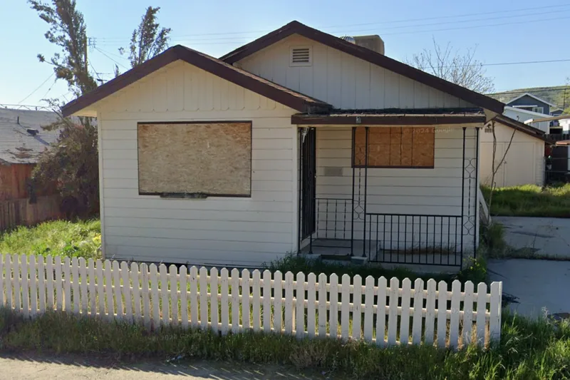 A boarded-up single-family home on the Kern County tax-sale list, windows sheeted over behind a picket fence