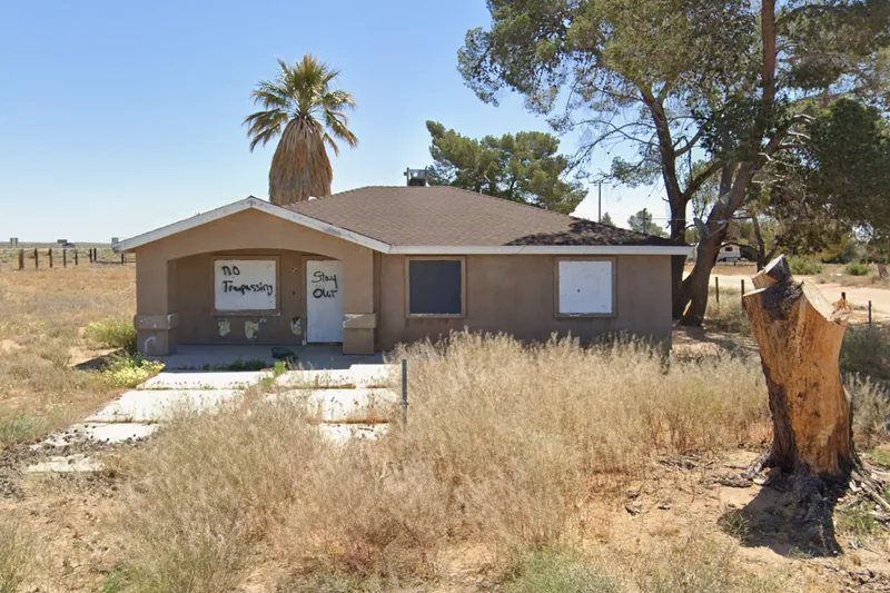 An abandoned house on the Kern County tax-sale list, boarded and posted against trespassers, surrounded by dry brush