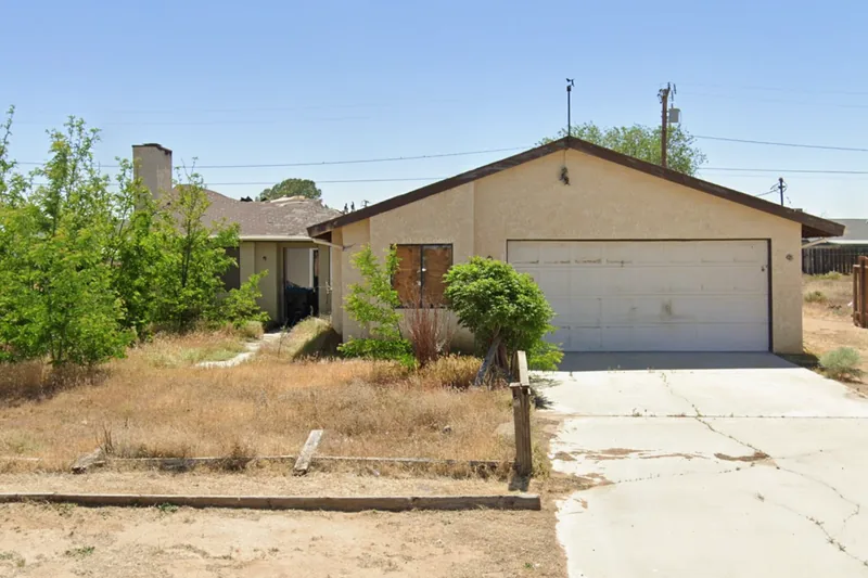 A vacant home on the Kern County tax-sale list with a boarded front window and long-dead landscaping